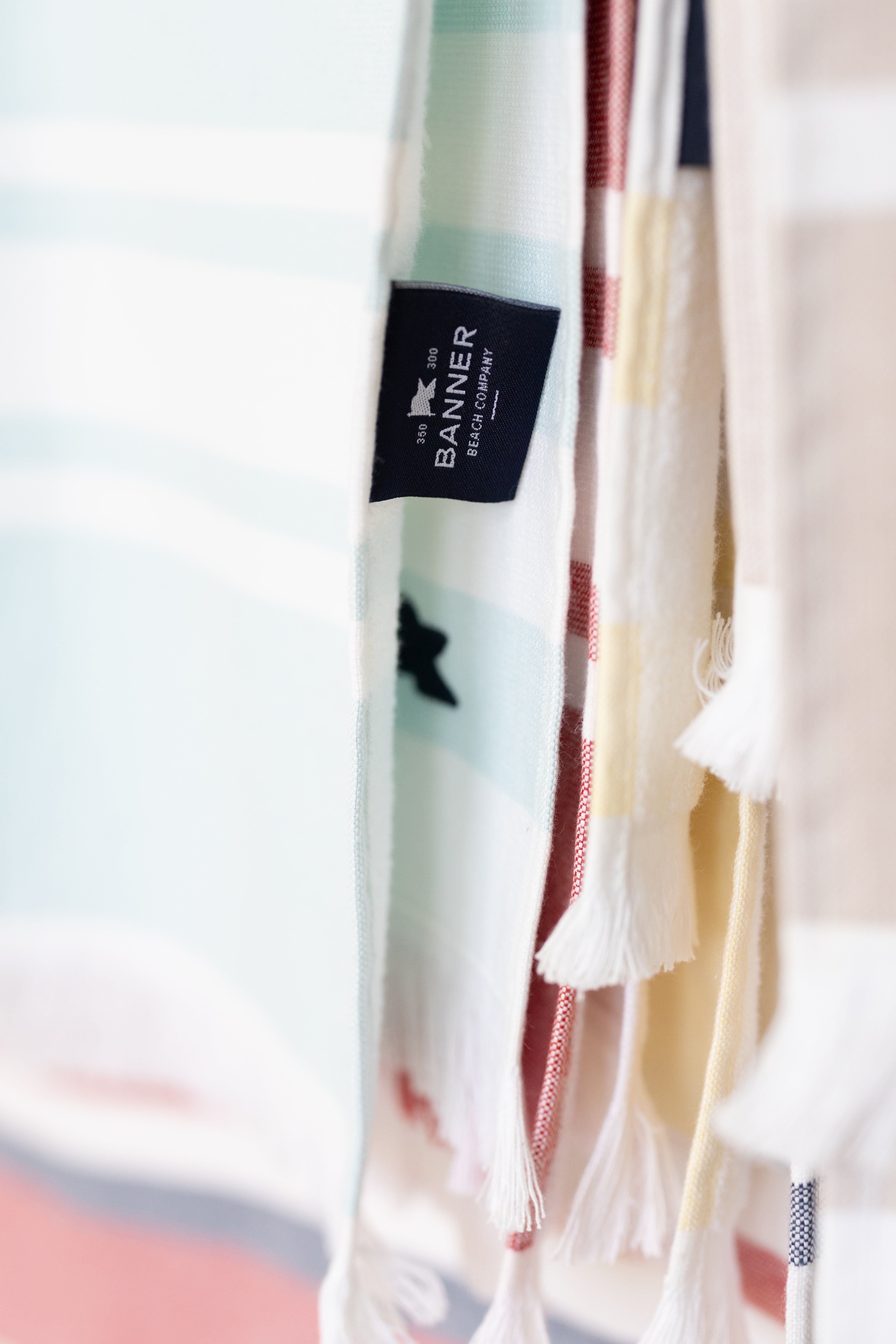 Colorful beach towels with a Banner Beach Towel brand label on a blurred background.