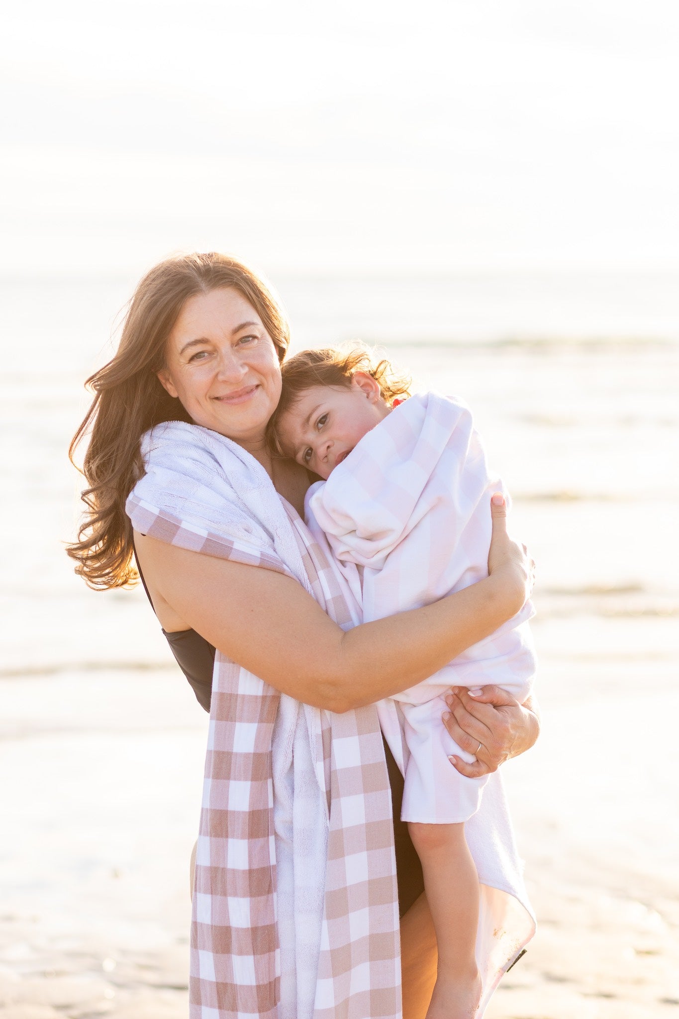 Woman holding a child wrapped in a beautiful towel on a beach